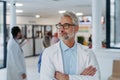 Portrait of confident mature doctor standing in Hospital corridor. Handsome doctor with gray hair wearing white coat Royalty Free Stock Photo