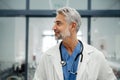 Portrait of confident mature doctor standing in Hospital corridor. Handsome doctor with gray hair wearing white coat Royalty Free Stock Photo