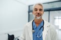 Portrait of confident mature doctor standing in Hospital corridor. Handsome doctor with gray hair wearing white coat Royalty Free Stock Photo