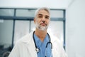 Portrait of confident mature doctor standing in Hospital corridor. Handsome doctor with gray hair wearing white coat Royalty Free Stock Photo