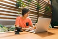 Portrait of confident mature professional woman in glasses, a coral T-shirt sitting on summer terrace in cafe, using laptop Royalty Free Stock Photo