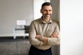 Portrait of confident middle aged businessman standing in office hall, posing with crossed hands and leaning on wall Royalty Free Stock Photo