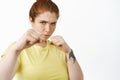 Portrait of confident redhead plus size girl boxing, punching with clenched fists, standing in defensive boxer pose