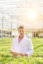 Portrait of confident scientist standing with clipboard amidst herbs in greenhouse