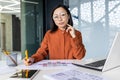Portrait of confident serious asian business woman financier inside office at workplace, worker behind paperwork looking