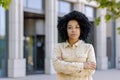 Portrait of confident serious business woman outside office building, aro american woman with crossed arms looking at Royalty Free Stock Photo