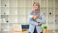 A confident Asian Muslim businesswoman stands in her office with a coffee cup in her hands Royalty Free Stock Photo