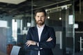 Portrait of confident smiling middle aged businessman in formal wear posing with crossed hands in office interior Royalty Free Stock Photo