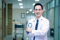 Portrait of confident smiling senior Asian male doctor in white workwear holding stethoscope and looking at camera, standing with Royalty Free Stock Photo