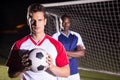 Portrait of confident soccer player holding ball with rival athlete