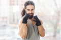 Portrait of confident sporty young adult muscular trainer man with curly long hair standing with raised heavy arms, holding fists