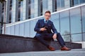 Portrait of a confident stylish businessman dressed in an elegant suit holds a smartphone and looking at camera while Royalty Free Stock Photo