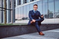 Portrait of a confident stylish businessman dressed in an elegant suit holds a smartphone and looking at camera while Royalty Free Stock Photo