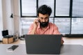 Portrait of confident successful Indian business man in casual clothes sitting at desk with laptop looking at camera in Royalty Free Stock Photo