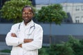 Portrait of a confident and successful young African American male doctor. He stands outside the hospital in a white Royalty Free Stock Photo