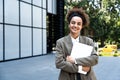 Portrait of confident successful young curly woman, formally dressed, business woman standing with laptop outdoors against the