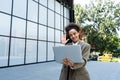 Portrait of confident successful young curly woman, formally dressed, business woman standing with laptop outdoors against the Royalty Free Stock Photo