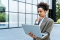 Portrait of confident successful young curly woman, formally dressed, business woman standing with laptop outdoors against the Royalty Free Stock Photo