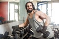 Portrait of confident young adult man handsome athlete with long curly hair working out in gym, standing, holding one dumbbell Royalty Free Stock Photo