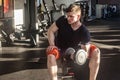 Portrait of confident young adult man handsome athlete working out in gym, sitting on a bench and holding one dumbbell with raised Royalty Free Stock Photo