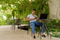 Portrait of young African businessman wearing casual clothes and sitting at coffee shop while using laptop computer and Royalty Free Stock Photo