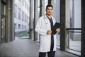Indian male medical doctor in white coat, standing with clipboard in hands outdoor Royalty Free Stock Photo