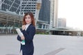 Portrait of confident young Asian business woman with ring binder standing at walkway of urban building background. Royalty Free Stock Photo