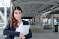 Portrait of confident young Asian business woman standing and holding document folder in her hands at walkway against copy space b Royalty Free Stock Photo