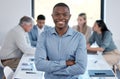 Portrait of a confident young businessman standing with his arms crossed in an office while his colleagues have a Royalty Free Stock Photo