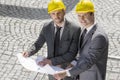 Portrait of confident young businessmen in hard hats examining blueprint outdoors