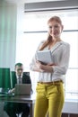 Portrait of confident young businesswoman holding digital tablet with businessman in background at office Royalty Free Stock Photo