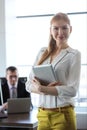 Portrait of confident young businesswoman holding tablet PC with businessman in background at office Royalty Free Stock Photo