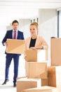 Portrait of confident young businesswoman standing by stacked boxes with male colleague in background at office Royalty Free Stock Photo