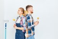 Smiling couple painting at home, holding paint roller and brush 