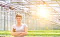 Portrait of confident young female botanist standing with arms crossed against herbs in greenhouse