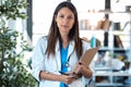 Confident young female doctor looking at camera while holding a clipboard and standing in the consultation Royalty Free Stock Photo