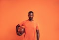 Portrait of a confident young man holding a basket ball against an orange background Royalty Free Stock Photo