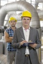 Portrait of confident young manager writing on clipboard with manual worker in background at industry Royalty Free Stock Photo