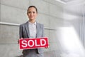 Portrait of confident young saleswoman holding sold placard against wall in apartment