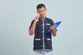 Portrait of confused asian young man wearing karate uniform holding clipboard and pen with pen Royalty Free Stock Photo