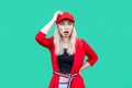 Portrait of confused blond young hipster woman in red blouse, cap, standing with hand on waist and on head looking away shocked,