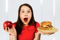 Portrait confused choice think person holds burger and red apple and surprised