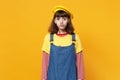 Portrait of confused cute girl teenager in french beret and denim sundress blowing lips isolated on yellow wall