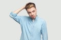 Portrait of confused handsome young man in light blue shirt standing, scratching his head, looking away and thinking what to do Royalty Free Stock Photo