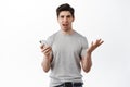 Portrait of confused man with smartphone, holding phone and complaining something strange, standing puzzled about online