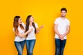 Portrait of confused person looking at funny girls teasing wearing white t-shirt denim jeans isolated over yellow