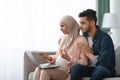 Portrait Of Confused Pregnant Muslim Couple Looking At Laptop Screen At Home