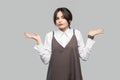 Portrait of confused thoughtful beautiful young woman in white shirt, brown apron with makeup and collected hair standing with Royalty Free Stock Photo