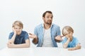 Portrait of confused unaware european father sitting with sons at table, shrugging with spread palms and questioned