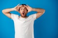 Portrait of a confused young man holding hands on his head over blue background Royalty Free Stock Photo